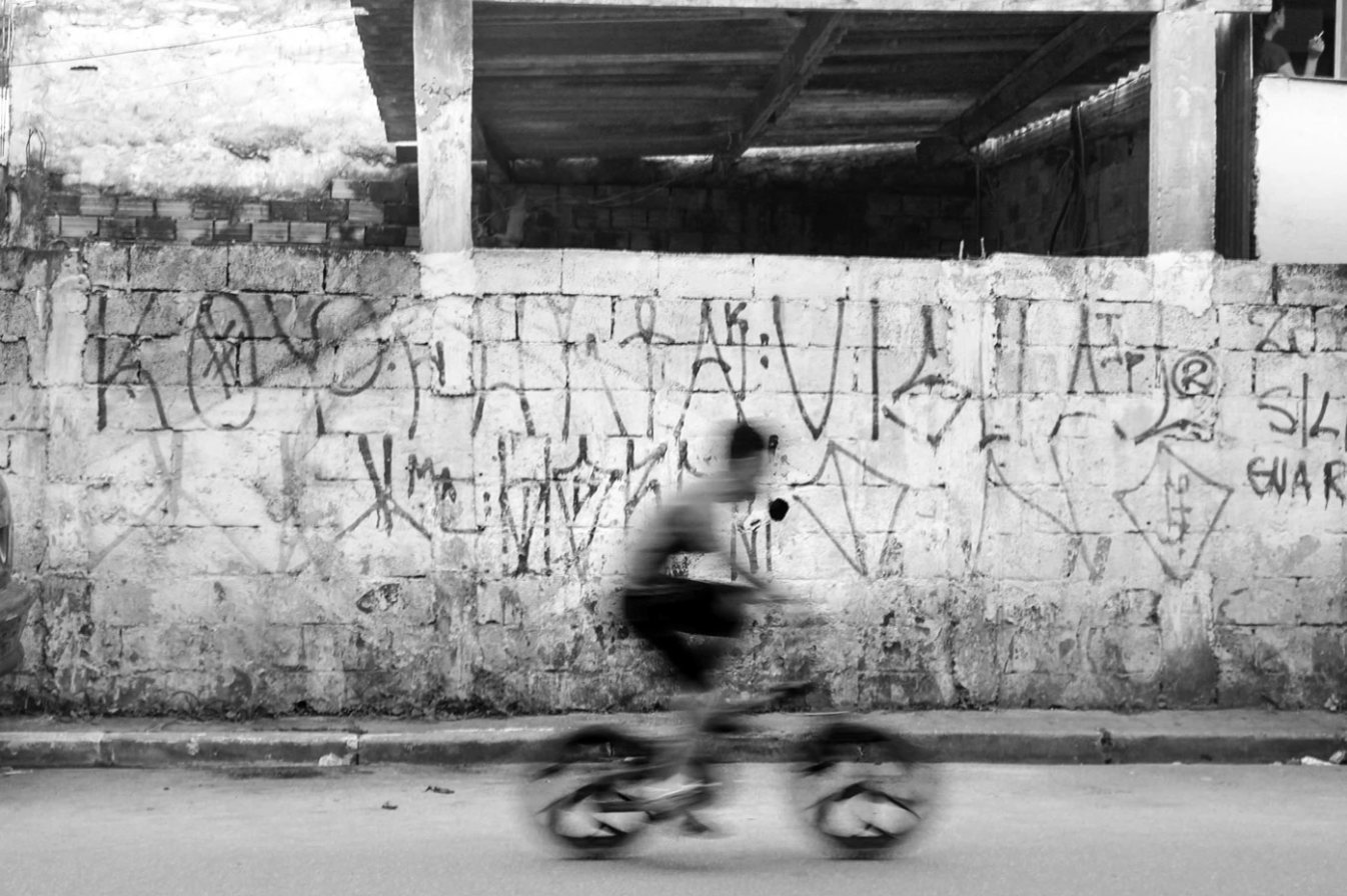Ciclista em movimento diante de um muro grafitado, em preto e branco