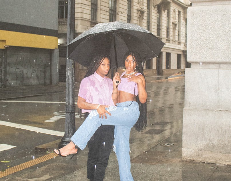 Duas pessoas sob um guarda-chuva preto em uma rua chuvosa de São Paulo